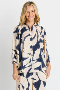 A woman modeling a matching two-piece lounge set featuring a long-sleeve button-up shirt and pants in a navy blue and cream abstract pattern, set against a plain light gray studio background.