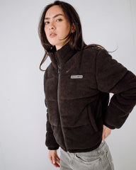 Person wearing a brown puffer jacket with a visible brand logo on a white background