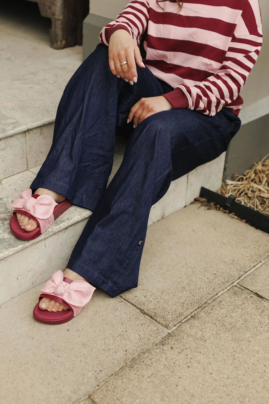 Person wearing a red and white striped sweater, navy pants, and pink sandals with bows sitting on steps.