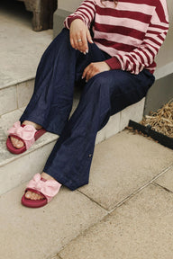 Person wearing a red and white striped sweater, navy pants, and pink sandals with bows sitting on steps.