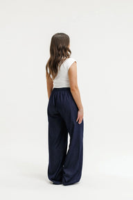 A woman shown from the back wearing a white sleeveless top and dark navy wide-leg trousers, standing against a plain white studio background.