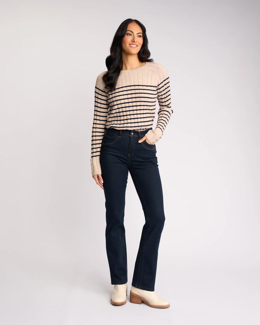 Woman wearing a striped sweater and dark jeans on a white background