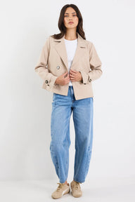 Woman wearing a beige blazer, white shirt, and blue jeans on a white background