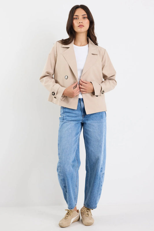 Woman wearing a beige blazer, white shirt, and blue jeans on a white background