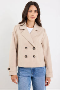 Woman wearing a beige double-breasted coat and blue jeans on a white background