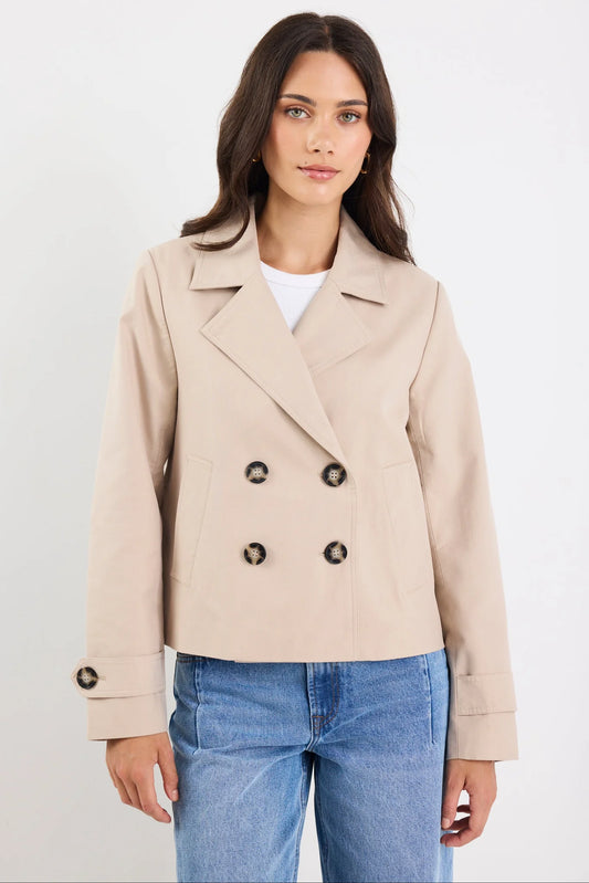 Woman wearing a beige double-breasted coat and blue jeans on a white background
