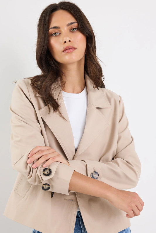 Woman wearing a beige blazer over a white shirt on a plain background