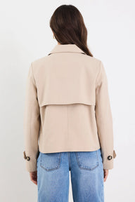 Person wearing a beige jacket and blue jeans on a white background