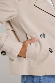 Close-up of a beige blazer with buttons and a hand in the pocket against a neutral background