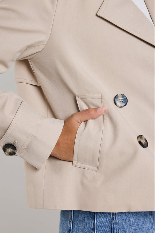 Close-up of a beige blazer with buttons and a hand in the pocket against a neutral background