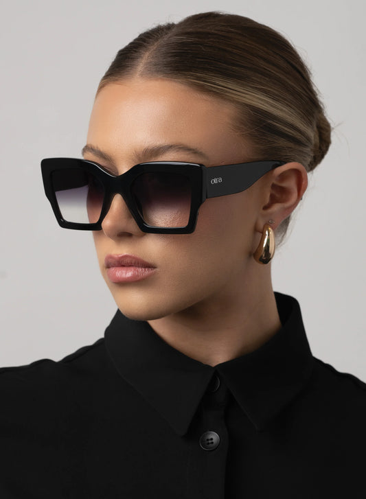 Person wearing black sunglasses and a black shirt against a gray background