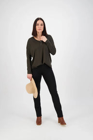 Woman wearing a green sweater and black pants holding a beige hat on a white background