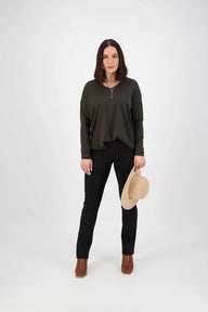 Woman wearing a green sweater and black pants holding a beige hat on a white background