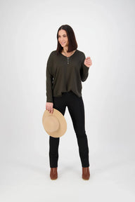 Woman holding a hat and wearing an olive green top and black pants on a white background