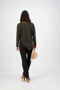 Woman wearing a long-sleeve olive green top and black pants, holding a beige hat on a white background