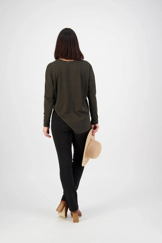 Woman wearing a long-sleeve olive green top and black pants, holding a beige hat on a white background