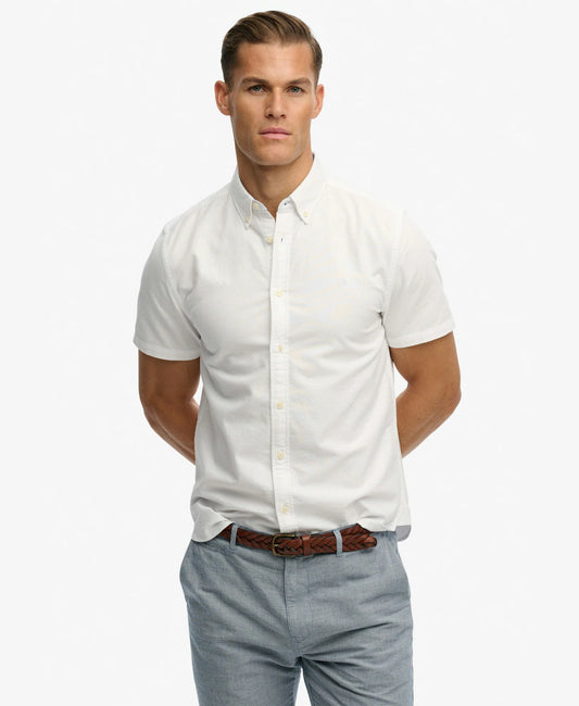 A man wearing a white short-sleeve button-down shirt, light blue jeans, and a brown woven belt, photographed against a clean white studio background.