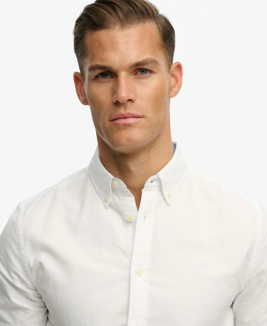 A close-up shot of a man wearing a white long-sleeve button-down shirt against a plain white background.