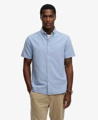 Man wearing a light blue short-sleeve shirt and beige pants on a white background