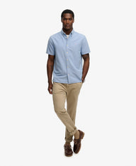 Man wearing a light blue short-sleeve shirt and beige pants on a white background