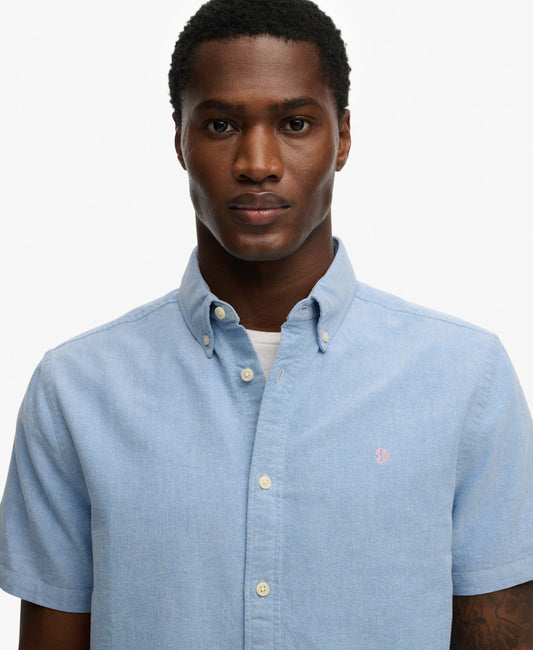 Man wearing a light blue button-up shirt with a small logo on a white background