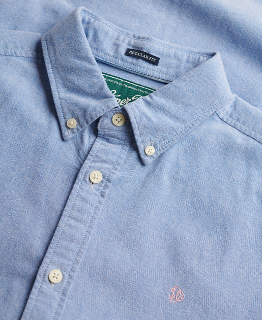 Close-up of a light blue shirt with collar and buttons, featuring a brand label.