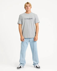 Person wearing a gray t-shirt with a quiksilver logo and light blue jeans on a white background