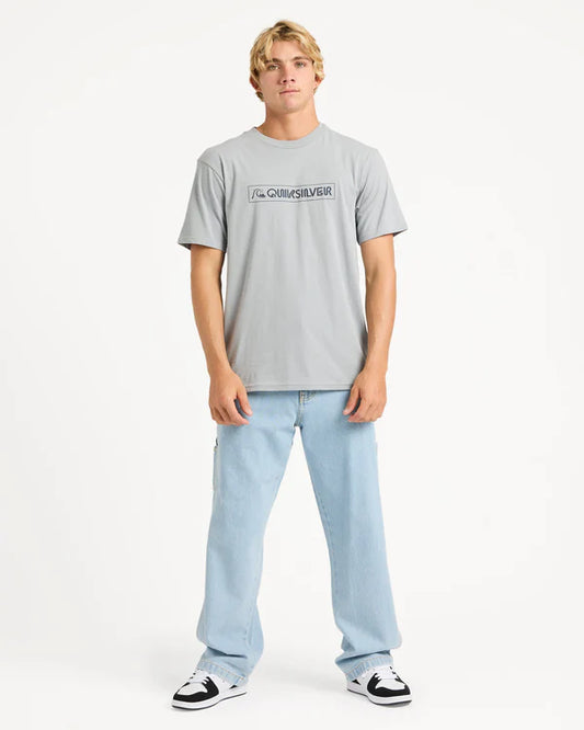 Person wearing a gray t-shirt with a quiksilver logo and light blue jeans on a white background
