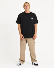 Person wearing a black t-shirt with a logo and beige pants on a white background