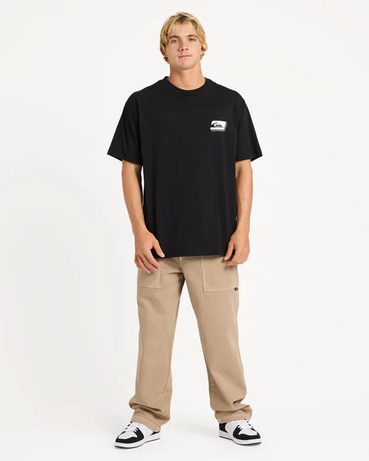 Person wearing a black t-shirt with a logo and beige pants on a white background