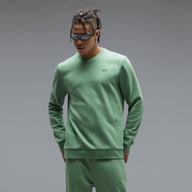 Man wearing a green sweatshirt and pants with sunglasses on a gray background