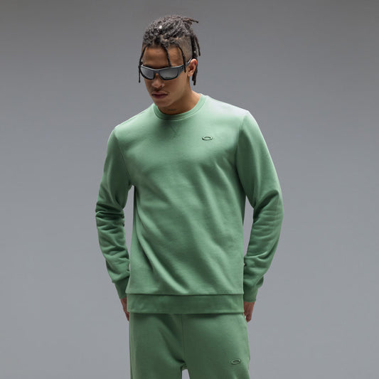 Man wearing a green sweatshirt and pants with sunglasses on a gray background