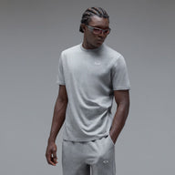 A man wearing a light gray short-sleeve crewneck t-shirt and matching gray sweatpants, featuring a small white Oakley logo on the chest and thigh, photographed against a neutral gray studio background.