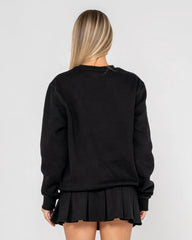 Person wearing a black sweatshirt and pleated skirt on a plain background
