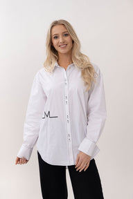 Woman wearing a white button-up shirt with a logo on a plain background
