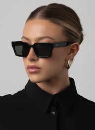 Woman wearing black sunglasses and a black shirt against a gray background