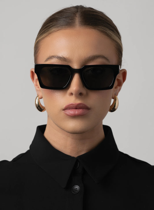 Woman wearing black sunglasses and a black outfit against a gray background