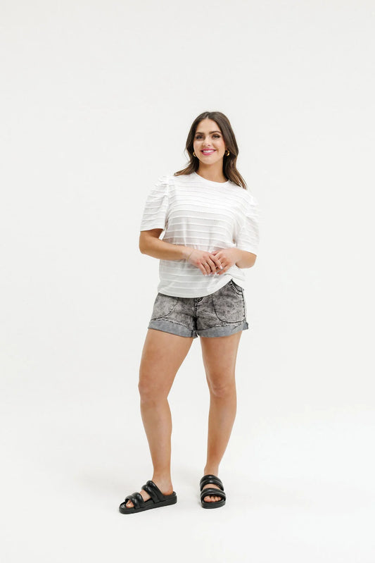 A woman modeling a white short-sleeve striped t-shirt, gray patterned shorts, and black slide sandals against a plain white studio background.