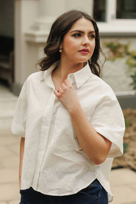 Woman wearing a white blouse with rolled-up sleeves outdoors.