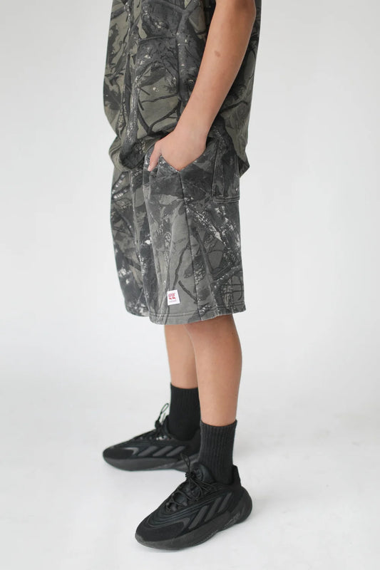 Person wearing camouflage shorts and black sneakers on a white background