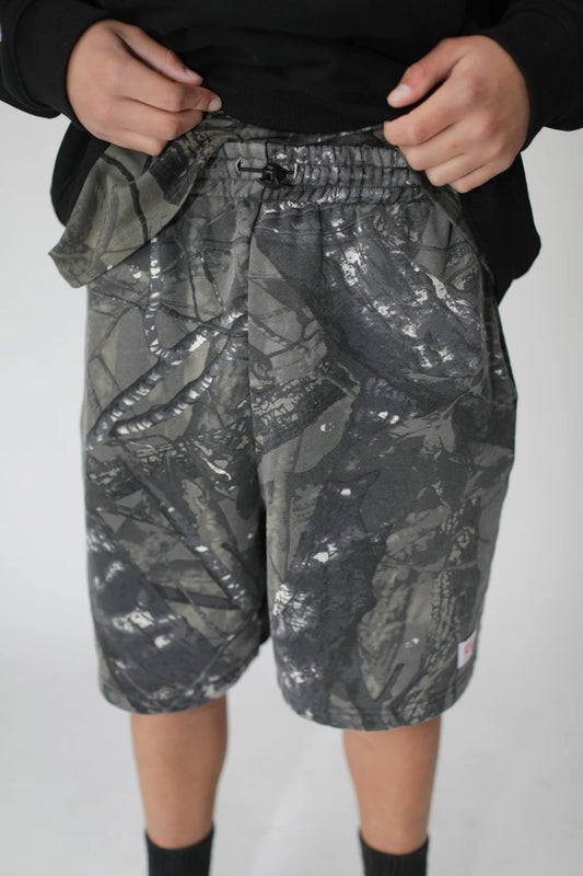 Person wearing gray camouflage shorts on a plain background