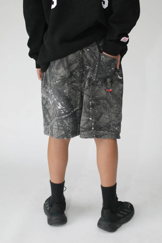 Person wearing camouflage shorts with a black sweatshirt on a white background