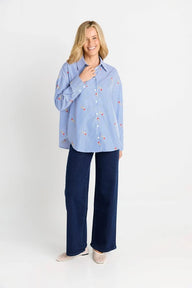 Woman wearing a light blue shirt with small patterns and dark blue pants on a white background