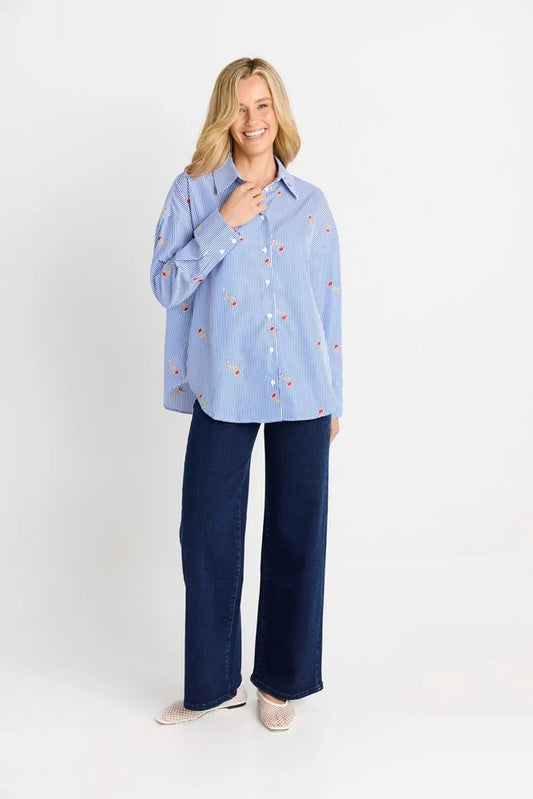 Woman wearing a light blue shirt with small patterns and dark blue pants on a white background