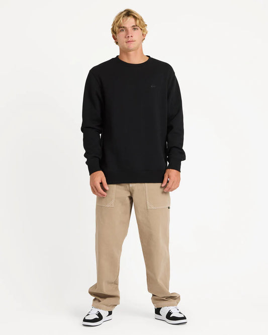 Man wearing a black sweatshirt and beige pants on a white background