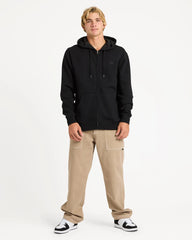 Person wearing a black hoodie and beige pants on a white background