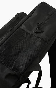 Close-up of a black backpack showing a front zippered pocket with a black zipper pull and a black mesh side pocket, photographed against a plain white background.