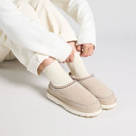 Person wearing beige slip-on shoes with white pants on a light gray background