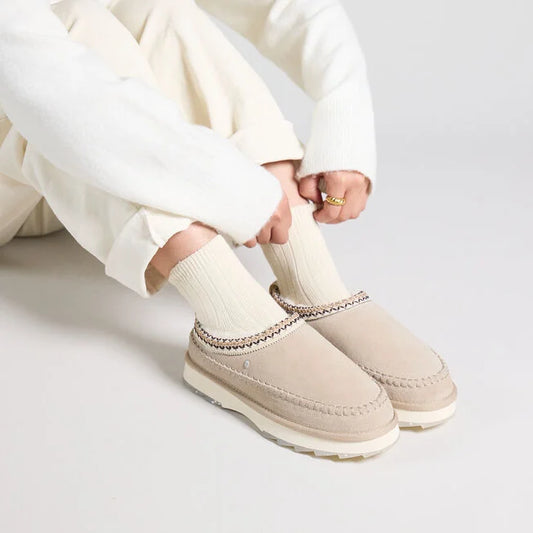 Person wearing beige slip-on shoes with white pants on a light gray background