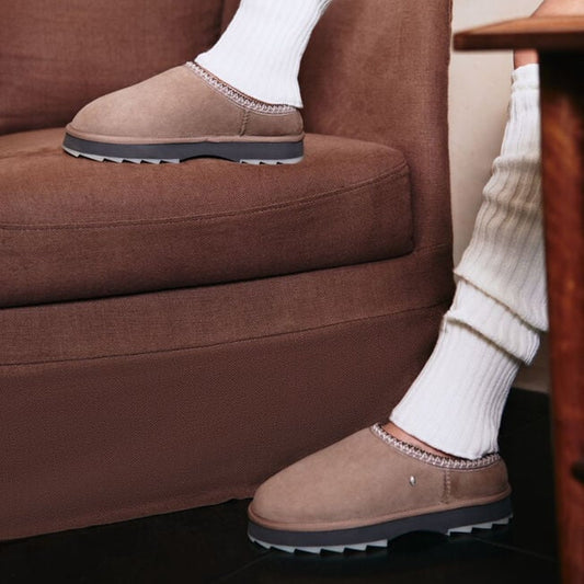 Brown slippers worn with white socks on a brown couch.
